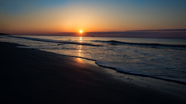 Ein Strand bei Sonnenuntergang, wo sanftes Wellenrauschen an die Küste schlägt.