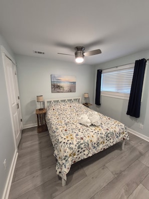 A bedroom with a bed, ceiling fan, bedside lamps, a painting, a window with curtains, and a door. - CLEAN, Convenient - fully renovated!  Sleeps 4   HHI STR#018944 (Hilton Head Island)