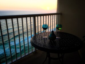 Ein Balkon mit Blick auf den Ozean bei Sonnenuntergang, mit einem Tisch, zwei Weingläsern und einer Vase.