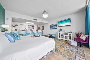 Ein Hotelzimmer mit einem großen Bett, einem Schreibtisch, einem Sessel, einem kleinen Tisch, einem farbenfrohen Teppich und Bildern an den Wänden.