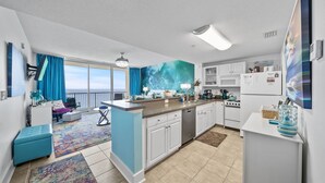 A modern kitchen with white cabinets, a central island, and a view to the outside. - Beachfront King Suite/Big Balcony! (Panama City Beach)