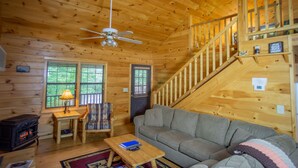 Ein gemütliches Blockhaus mit Holzeinrichtung, einer Couch, einem Tisch, einem Sessel, einem Kamin und einer Treppe.