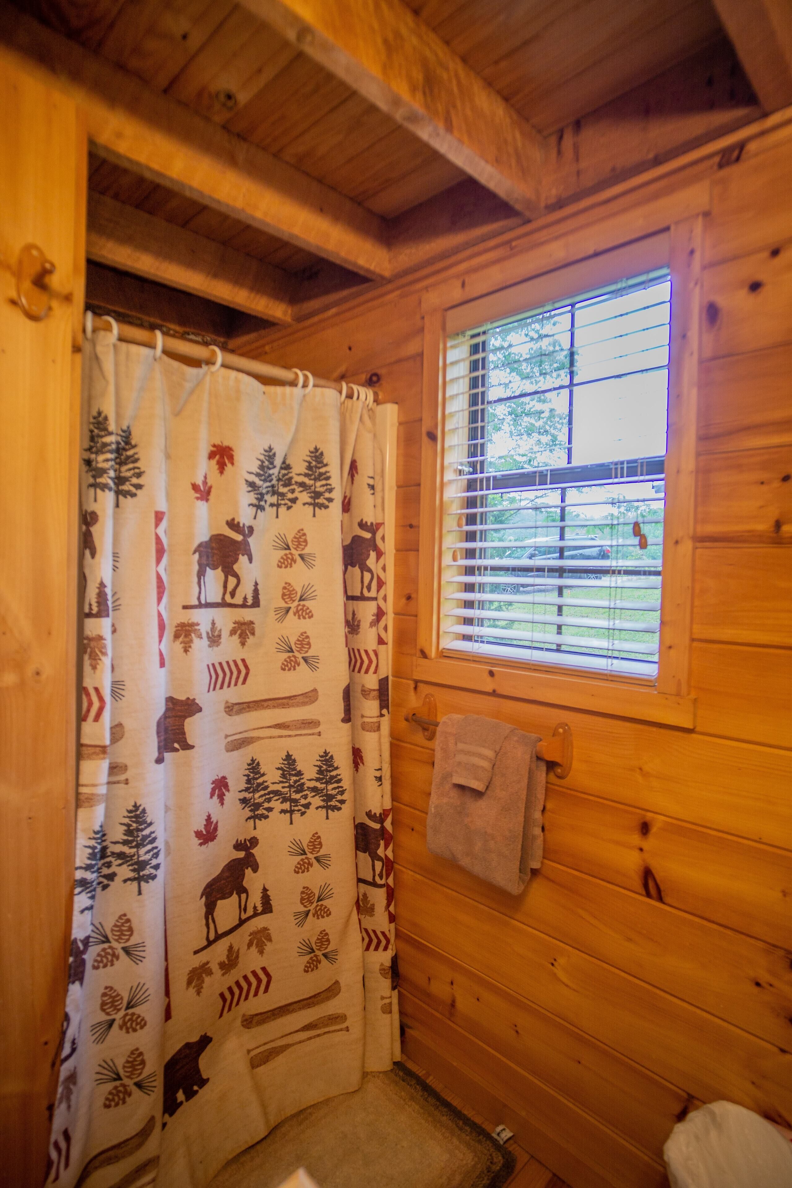 A wooden cabin bathroom with a window, a shower curtain with animal prints, and a towel hanging on the wall.