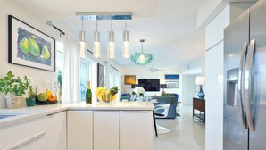 Eine moderne Küche mit Kochinsel, Pendelleuchten und einem großen Kühlschrank.