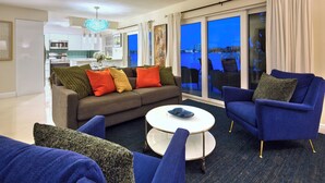 Ein modernes Wohnzimmer mit einer Couch, Sesseln und einem Couchtisch. Große Fenster bieten Blick auf die Stadt.