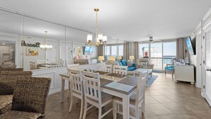 A spacious living area with a dining table, chairs, a sofa, and a TV. - 16th floor 2 bedroom Beachfront at Pelican. Stunning View, 3 Pools, Beach Chairs (Destin)