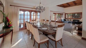 A dining area with a table set for six, surrounded by chairs, a chandelier, and large windows with curtains. - Overlooks Los Suenos Marina 5BR (Playa Herradura)