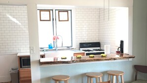 Une cuisine moderne avec des murs en briques blanches, un îlot central doté de tabourets et un coin repas avec une table et des chaises en bois.