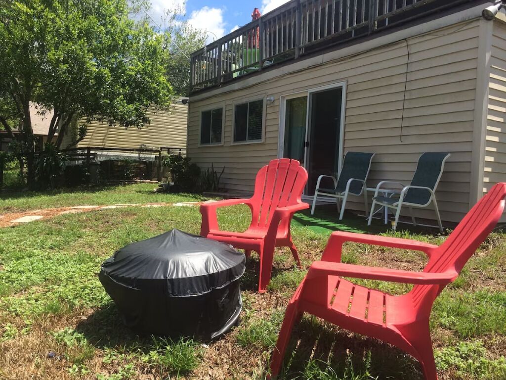 Un jardin avec un espace de détente extérieur abrité, un parasol et des chaises rouges.