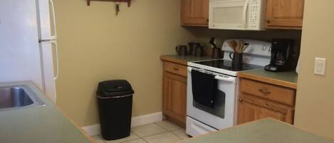 A compact kitchen with wooden cabinets, a white refrigerator, a microwave, and a stove.