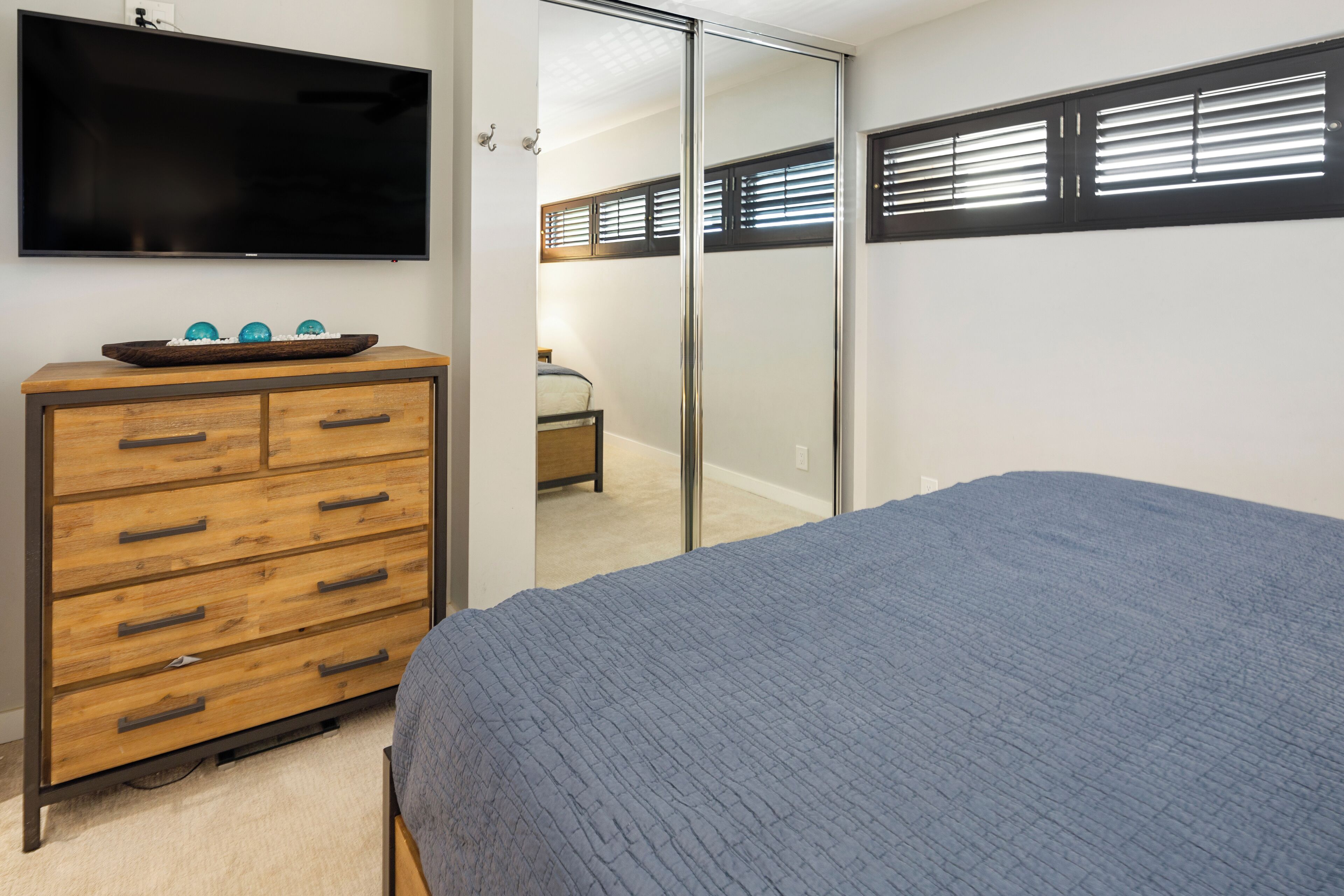 A bedroom with a bed, a wooden dresser with drawers, a flat-screen TV, and a sliding closet door.