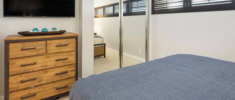 A bedroom with a bed, a wooden dresser with drawers, a flat-screen TV, and a sliding closet door.