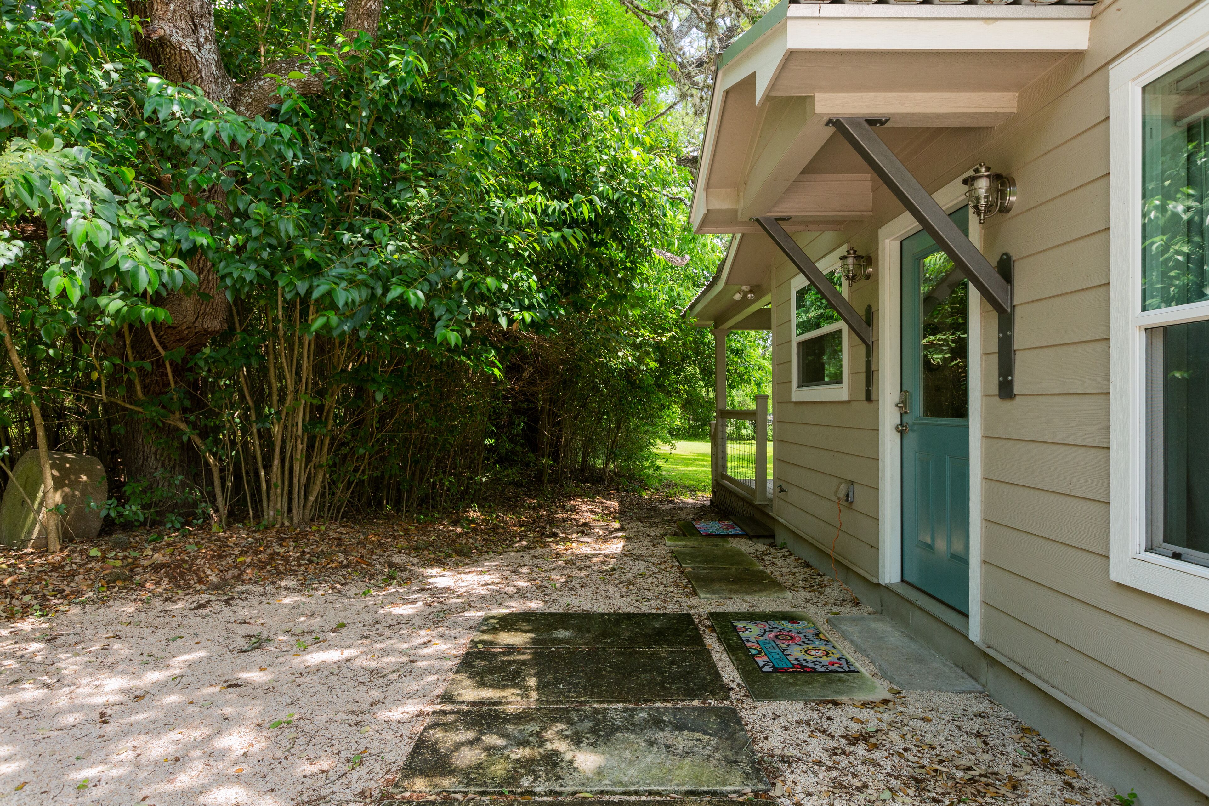 Een pad dat leidt naar een huis met een veranda, omringd door weelderige begroeiing.