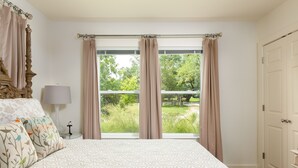 Un dormitorio con una cama grande, una mesita de noche, una lámpara y vistas a la vegetación exterior.