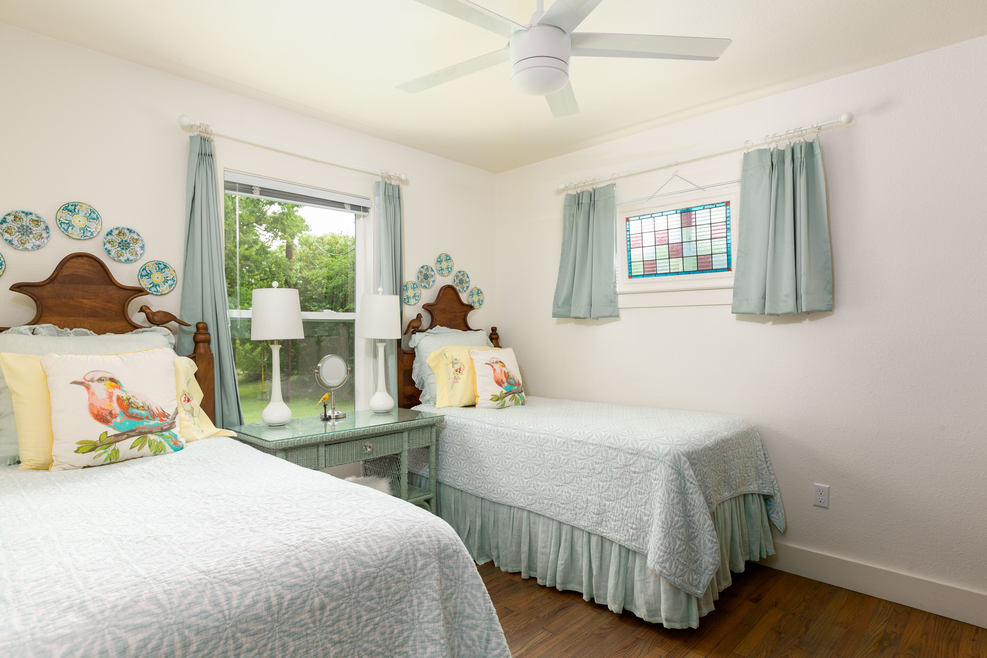 A bedroom with two beds, a ceiling fan, a window with curtains, and decorative plates on the wall.