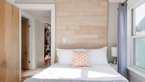 Una moderna camera d'albergo con un letto grande, una testiera in legno e vista sulla città attraverso una finestra.