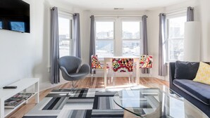 Un soggiorno moderno con un tavolino in vetro, una poltrona, una TV a parete e un'area pranzo con sedie e tavolo.