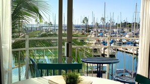 Un balcon offrant une vue sur une marina, avec plusieurs bateaux et des palmiers.