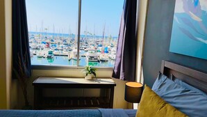 Une chambre d’hôtel avec un lit, une table de chevet avec une lampe et une fenêtre donnant sur une marina remplie de bateaux.