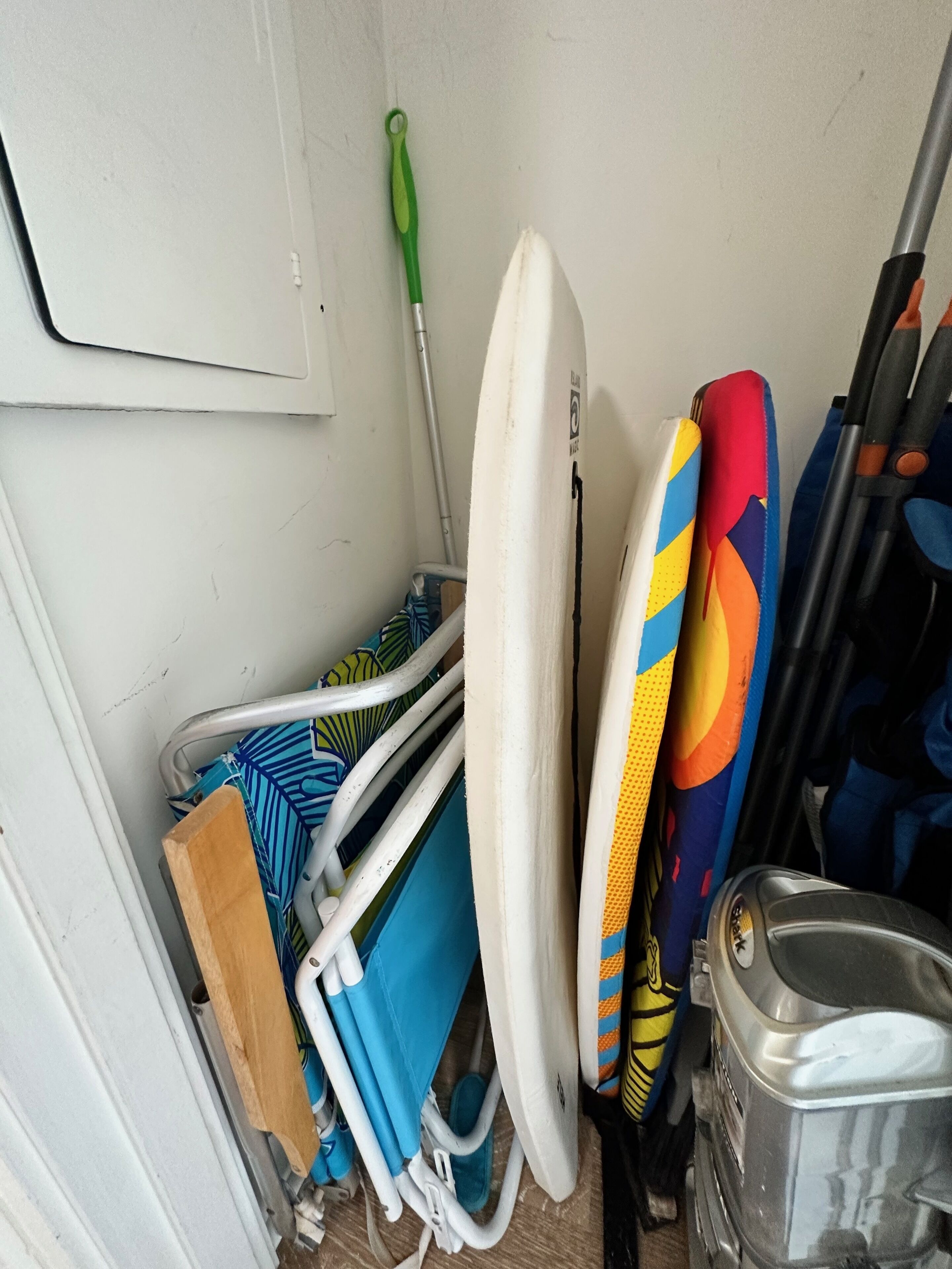 Un espace de rangement contenant divers objets, notamment une planche de surf, une serpillière et un récipient en métal.
