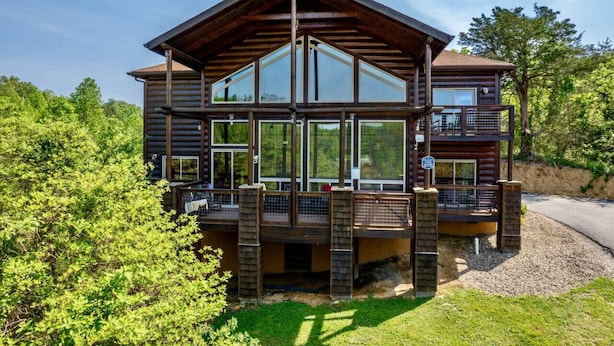 Une cabane en rondins dotée d’une grande terrasse, de nombreuses fenêtres et offrant une vue pittoresque sur la forêt environnante.