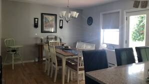 Un comedor con una mesa de madera, sillas, una araña y una ventana con persianas.