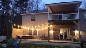 Una casa de dos pisos con un porche cubierto, mobiliario exterior y luces colgantes.