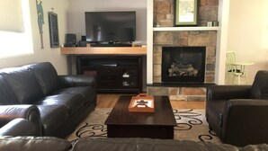Una sala de estar con chimenea, televisor de pantalla plana, sofás de cuero y una mesa de centro.