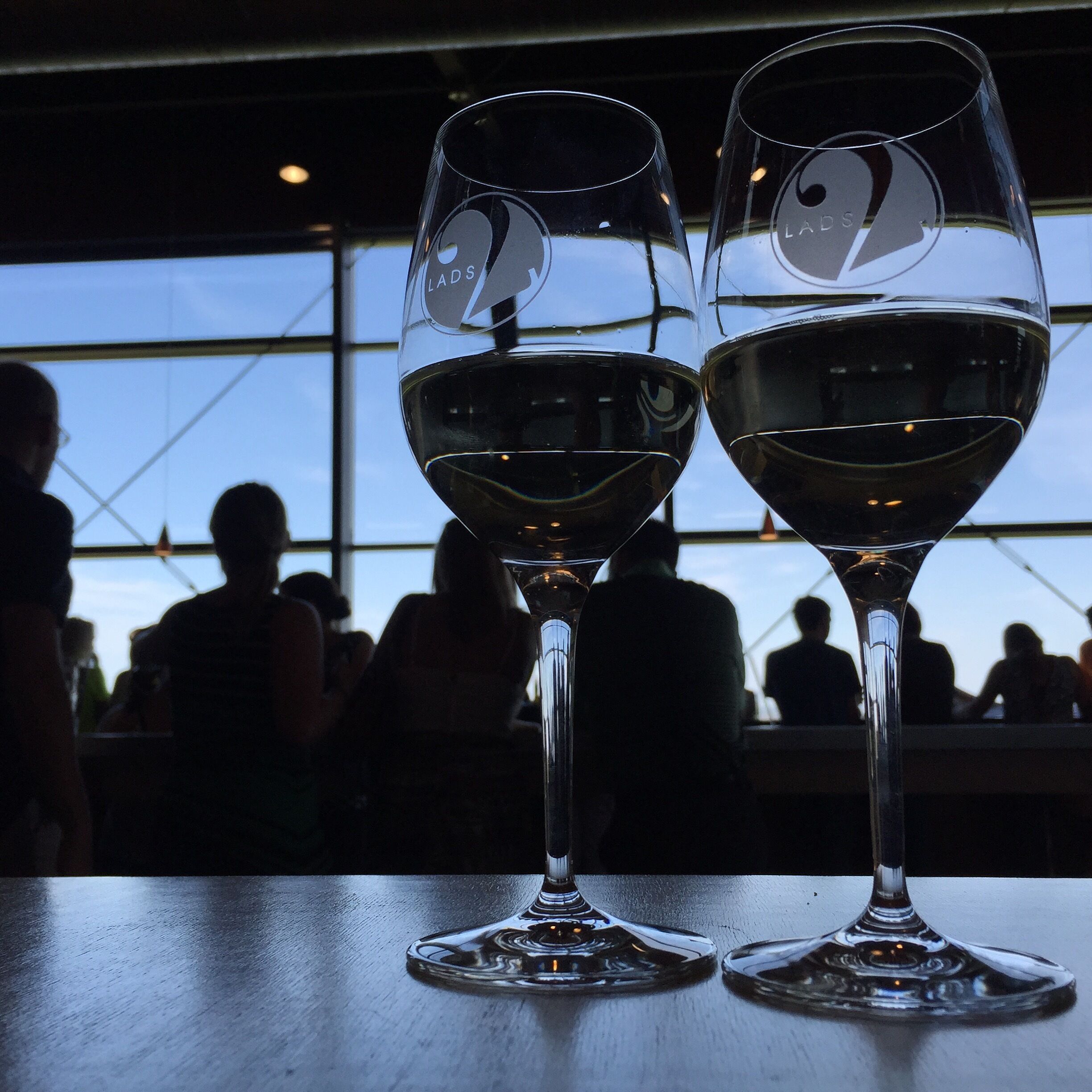 Deux verres à vin sont posés sur une table, et on aperçoit des personnes à l’arrière-plan.
