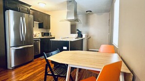 A compact kitchen with modern appliances, a dining table with chairs, and a window providing natural light. - Downtown Traverse City Condo. Great Location. New King Bed  (Traverse City)