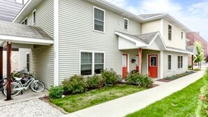 A two-story residential building with a covered front porch and a red door. - Downtown Traverse City Condo. Great Location. New King Bed  (Traverse City)