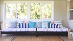 A room with a large window, a sofa with patterned cushions, and a woven basket.