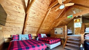 Una baita di legno con due letti, una ventola a soffitto e una scala.