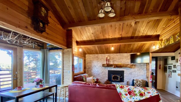 Un accogliente interno di una baita con soffitto in legno, un caminetto, un divano rosso e una zona pranzo con tavolo e sedie.