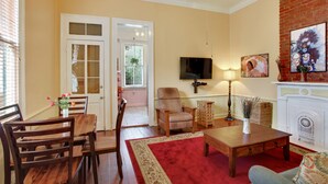 Un salon avec une table en bois, des chaises, un tapis rouge, une cheminée et un téléviseur fixé au mur.