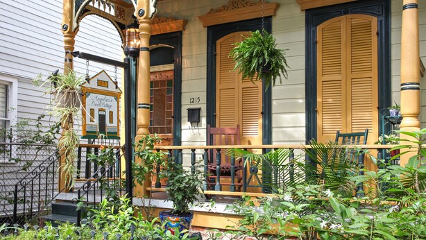 Une véranda avec une balustrade en bois, un banc et une plante suspendue.
