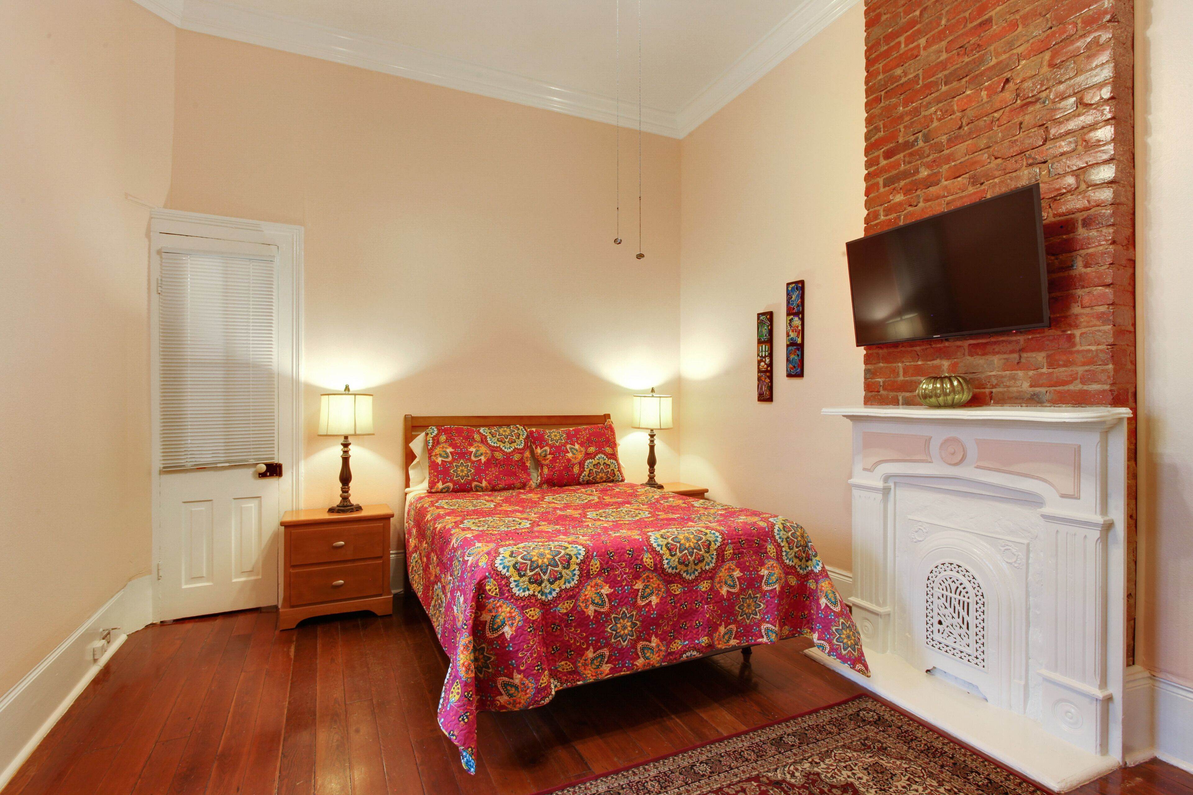 Een slaapkamer met een bed, nachtlampjes, een open haard en een aan de muur bevestigde televisie.