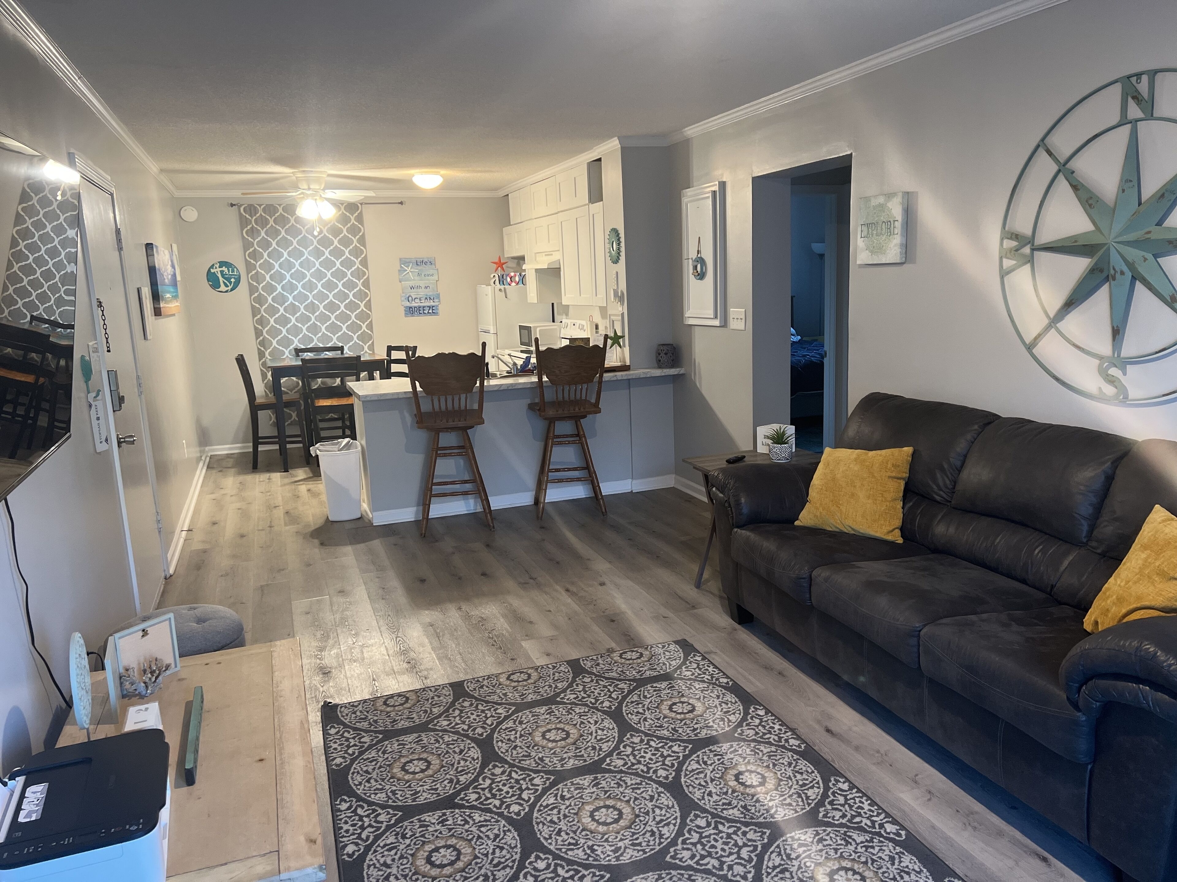 A modern living room with a dark leather sofa, a patterned rug, and a kitchen area in the background.
