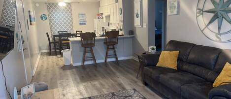 A modern living room with a dark leather sofa, a patterned rug, and a kitchen area in the background.