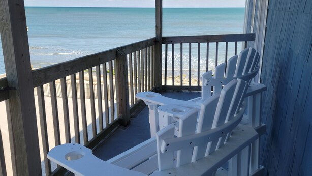 Una terrazza coperta con poltrone Adirondack bianche che si affacciano su una spiaggia.