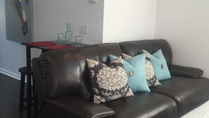 A dark leather sofa with patterned cushions, a small table with red and clear glassware, and a painting on the wall. - Mayfaire, 3 miles to Wrightsville Beach. Very convenient  (Wilmington)
