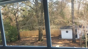 A view through a window of a backyard with a wooden fence, trees, and a small shed. - Mayfaire, 3 miles to Wrightsville Beach. Very convenient  (Wilmington)