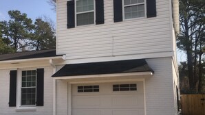 A two-story house with a garage, a black awning over the garage, and a statue of a person sitting on the ground in front of the house. - Mayfaire, 3 miles to Wrightsville Beach. Very convenient  (Wilmington)