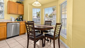 A kitchen with wooden cabinets, a dishwasher, a dining table with chairs, and a window with blinds. - Hakuna Ma'Cottage - Minecraft Room, Southern Pool! (Kissimmee)