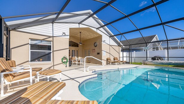 A covered swimming pool with lounge chairs, a ceiling fan, and a clock on the wall. - Hakuna Ma'Cottage - Minecraft Room, Southern Pool! (Kissimmee)