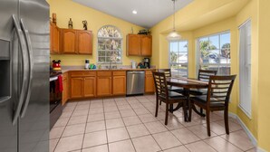 A kitchen with wooden cabinets, a stainless steel refrigerator, a dishwasher, and a dining table with chairs. - Hakuna Ma'Cottage - Minecraft Room, Southern Pool! (Kissimmee)
