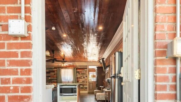 A wooden ceiling with a central light fixture, a kitchen with a refrigerator and a microwave, and a door leading to another room.