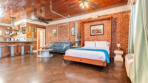 A spacious room with a large bed, a sofa, a dining area, and a kitchen.