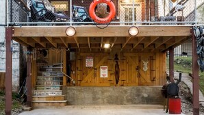 A two-story building with a wooden deck, a lifebuoy hanging from the railing, and a staircase leading to the entrance.