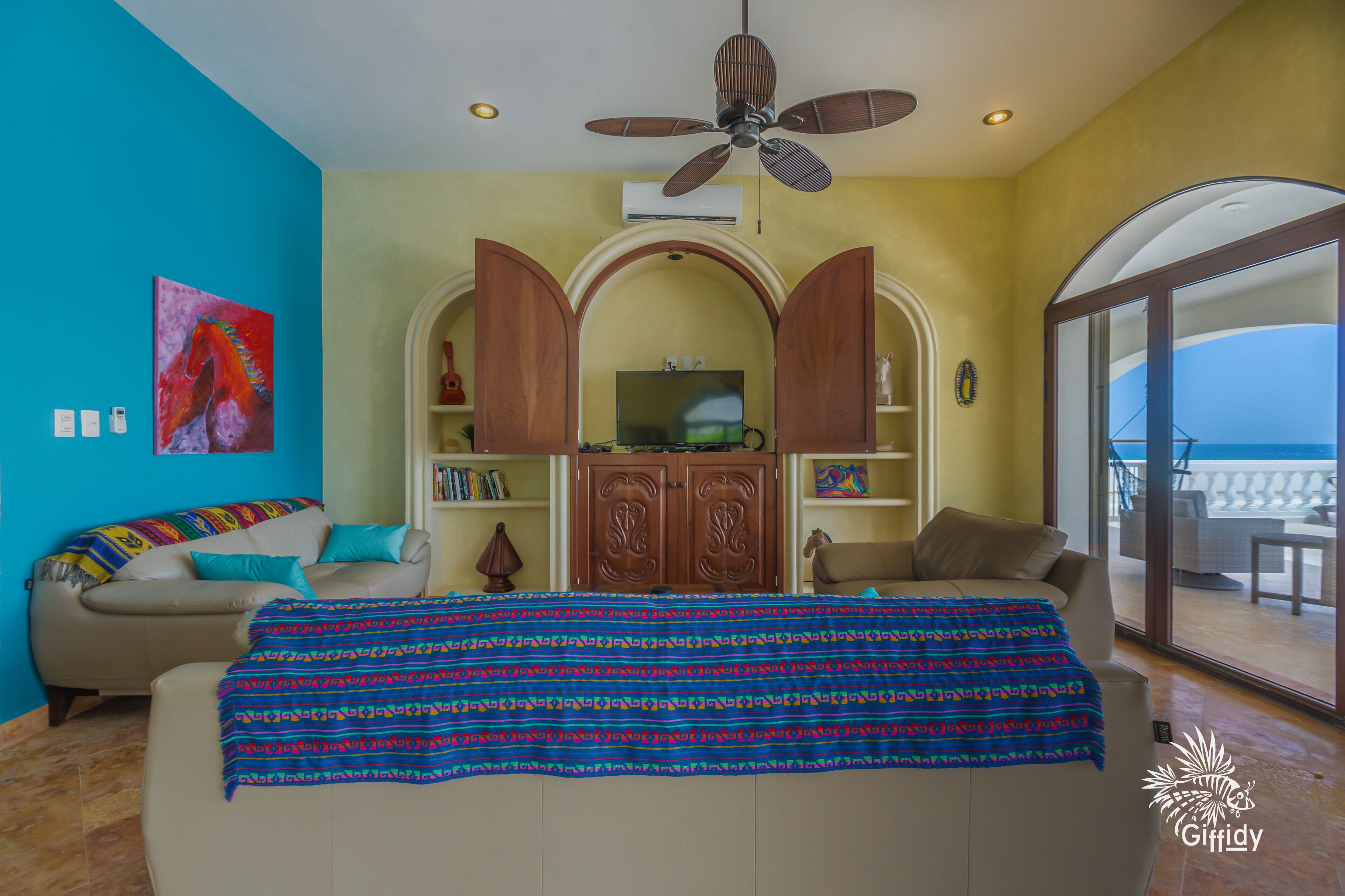 A spacious living room with a large bed, a television, and a balcony with a view of the sea.